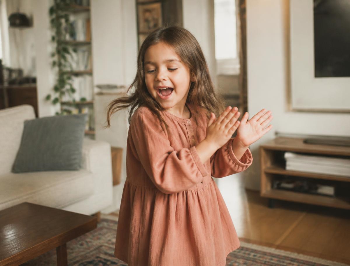 A young child singing and clapping along to music in a living room at home.